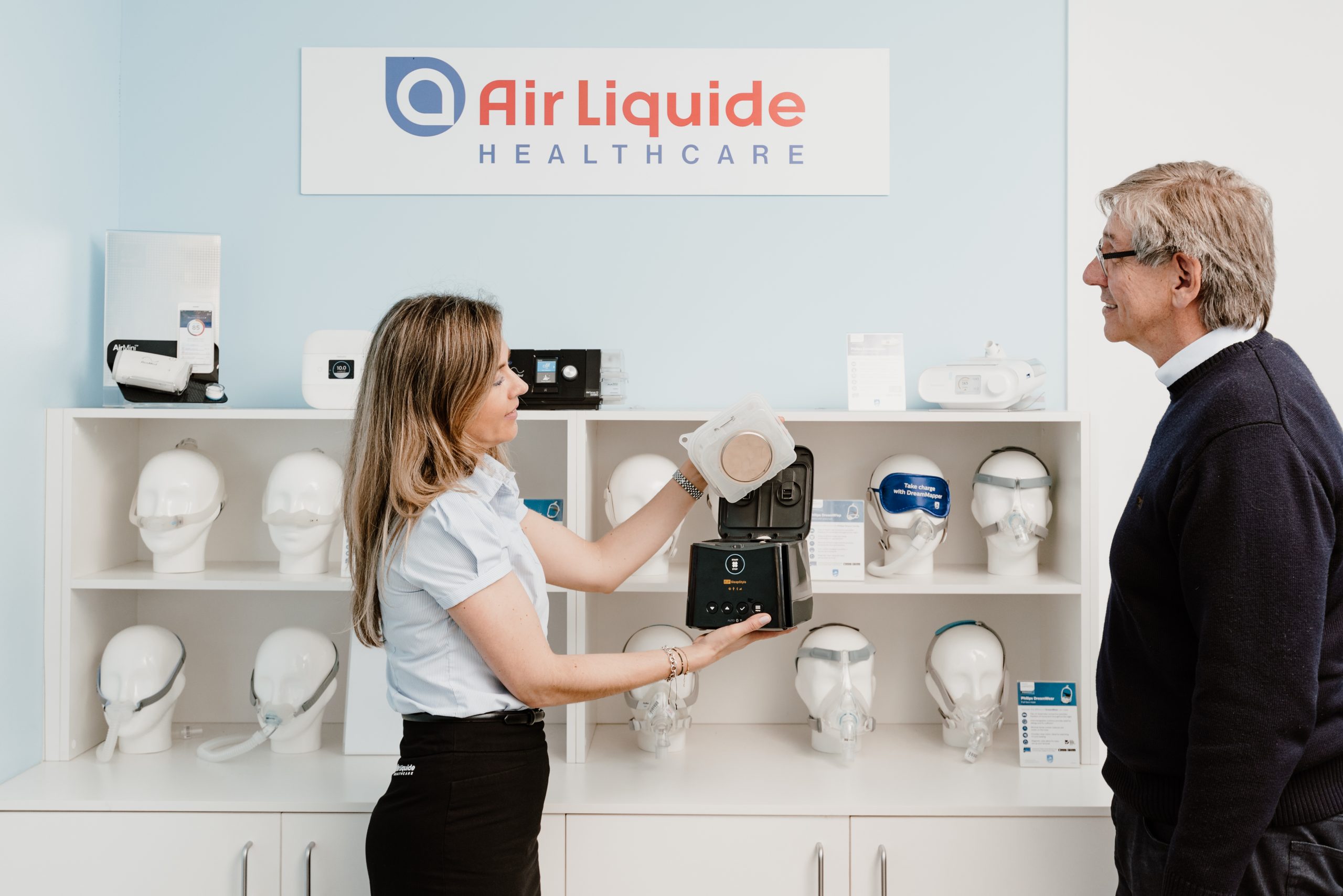 A sleep therapy consultant lifting the humidifier chamber out of a PAP machine to show a patient