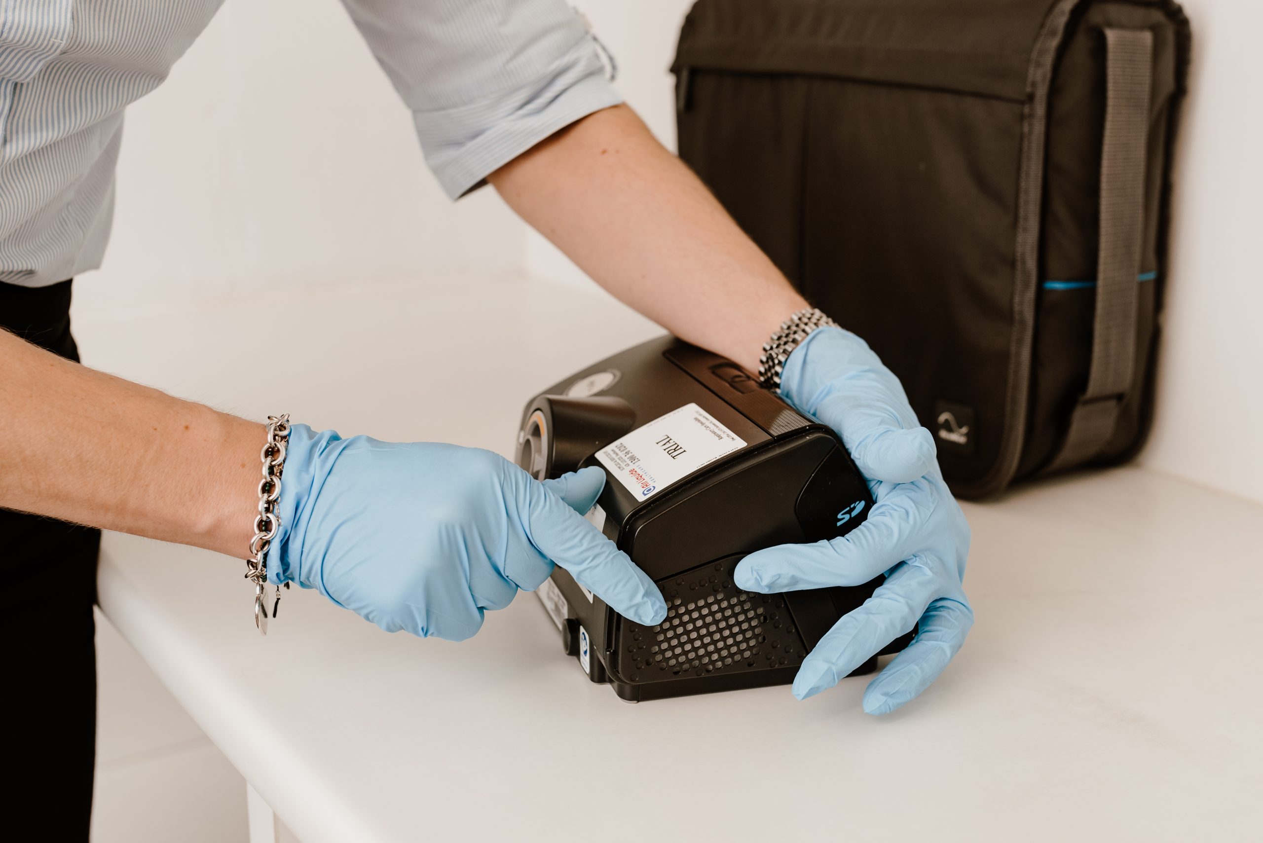 Gloved hands opening the air filter cover on the side of a PAP device sitting on a bench