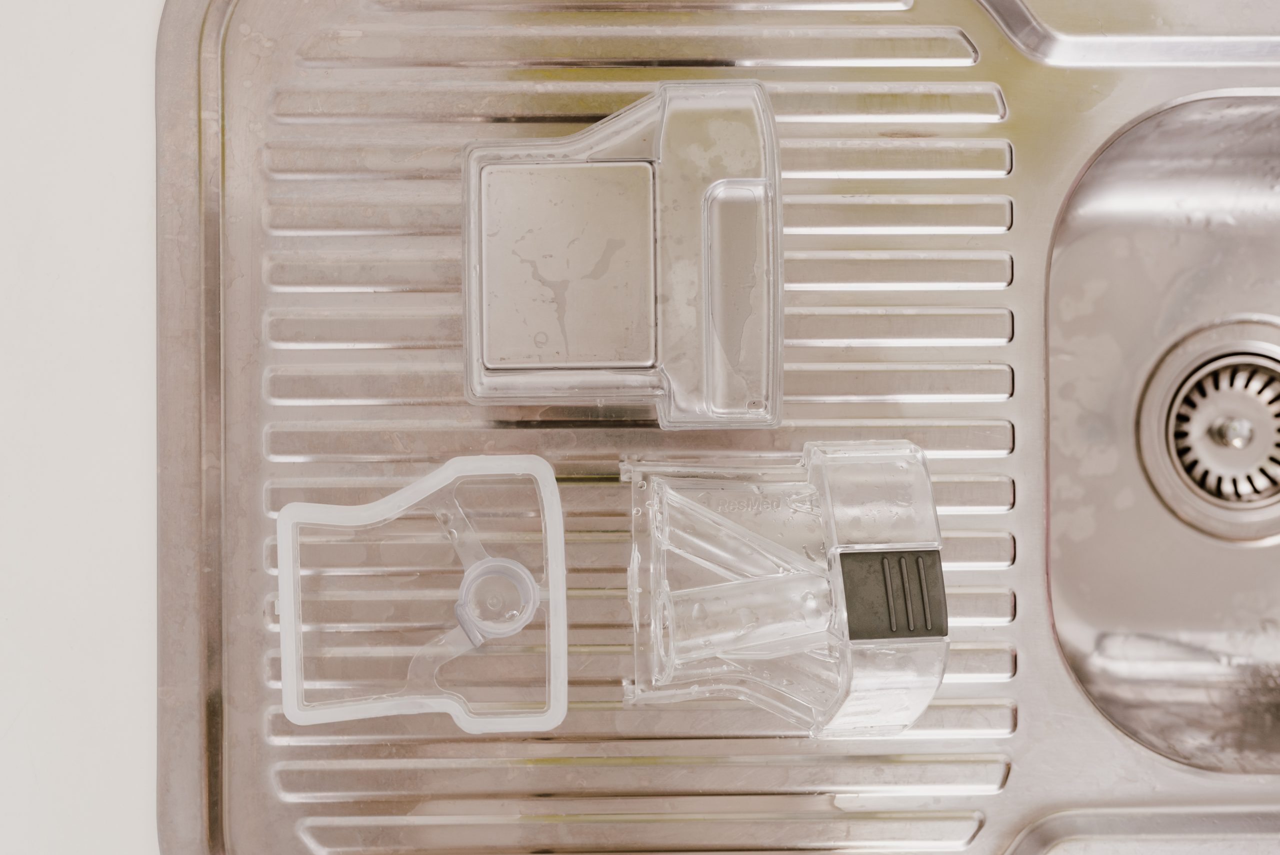 A humidifier chamber taken apart into its clear pieces, laid out to dry on a stainless steel draining board