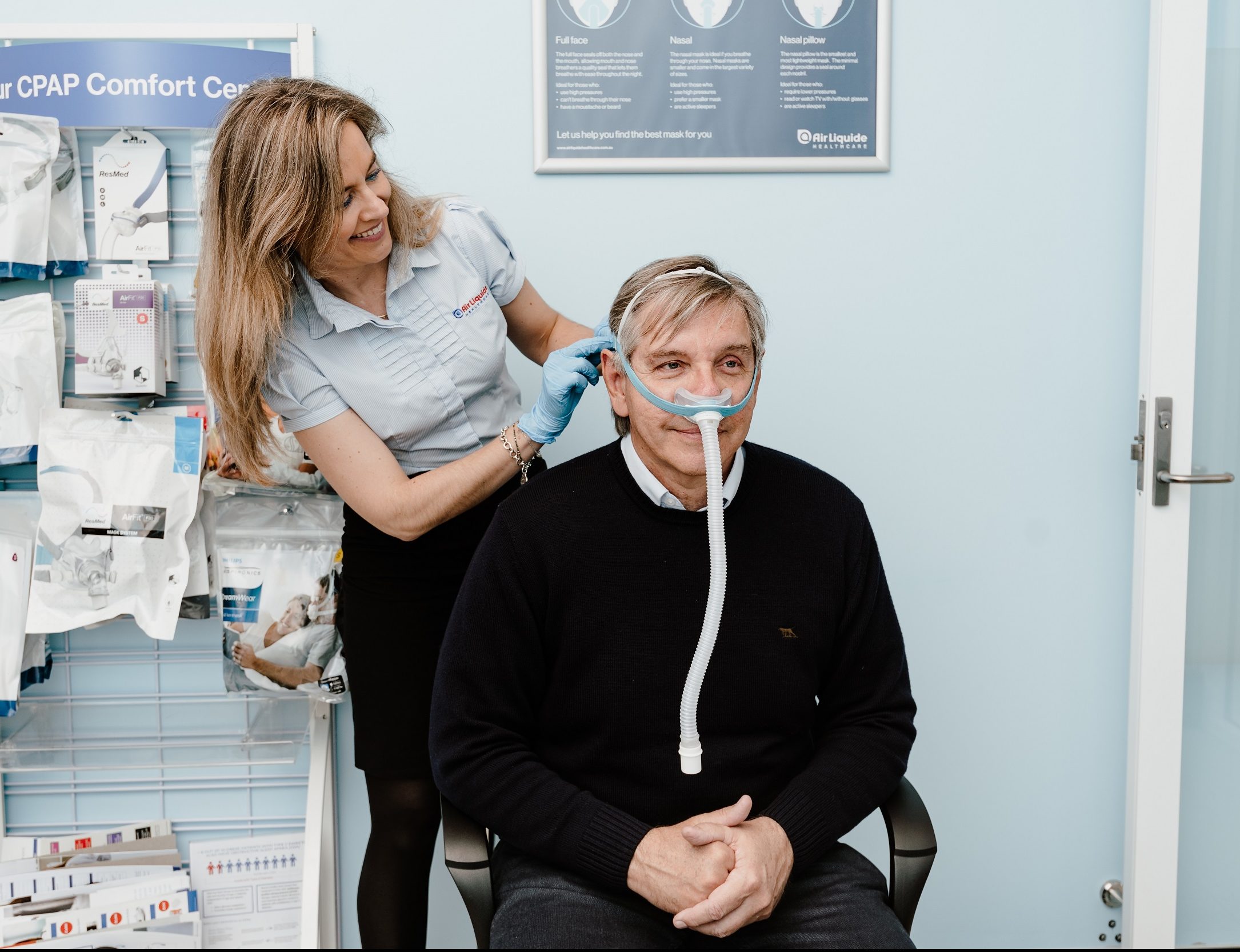 A sleep therapy consultant fitting a PAP mask to a patient in a clinic
